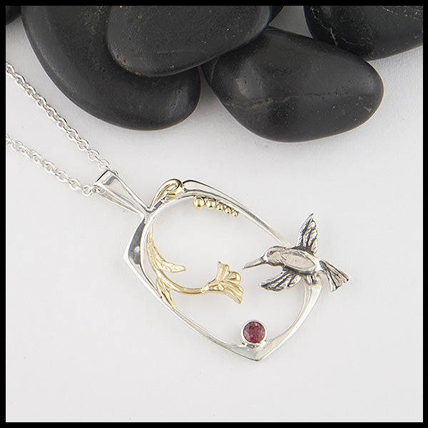 Custom Hummingbird pendant made in Sterling Silver and 14K Yellow Gold with a hummingbird, flower, and accent beads, set with a Rhodolite Garnet. 