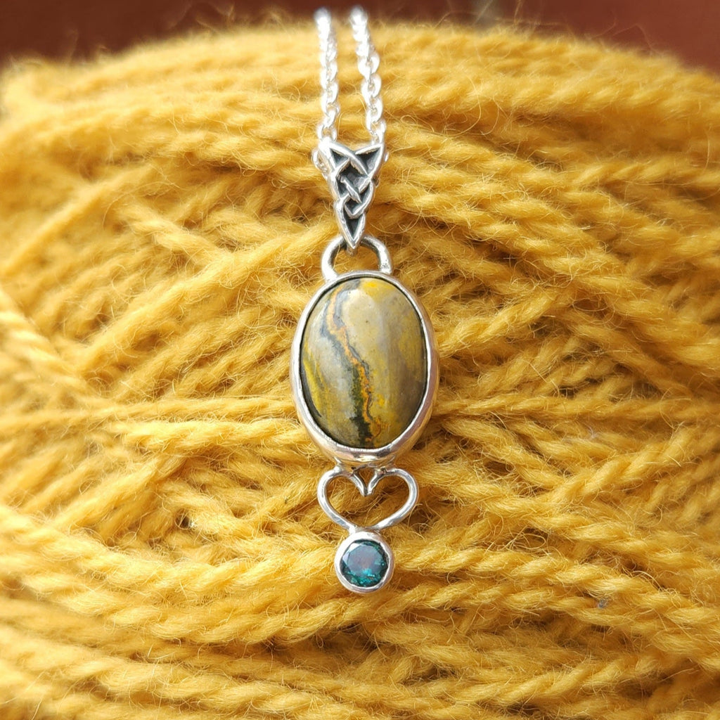 Silver pendant with a yellow Bumblebee Jasper and Evergreen Topaz on a yellow yarn background.