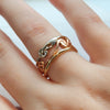 Gold ring with a wavy design on a person's finger against a neutral background