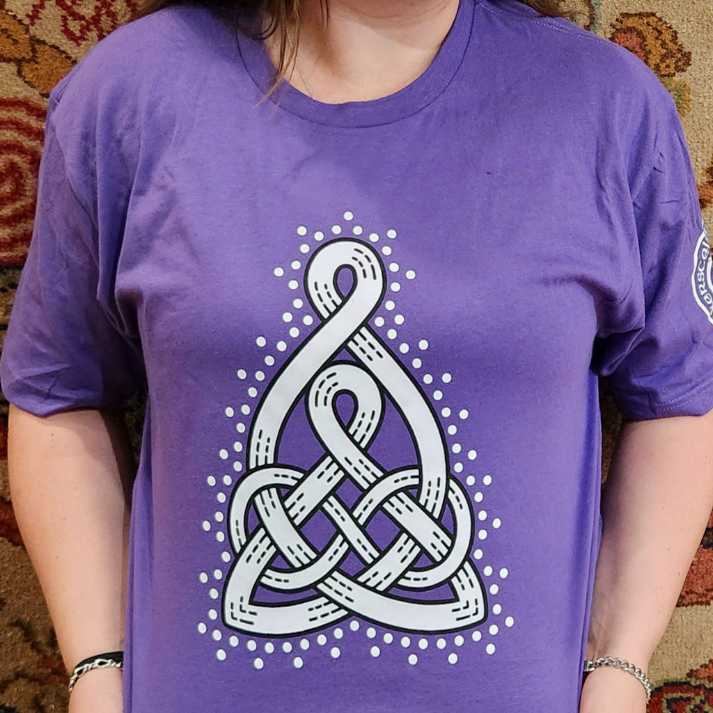 Person wearing a purple t-shirt with a white Celtic Mother's knot design on a patterned carpet background