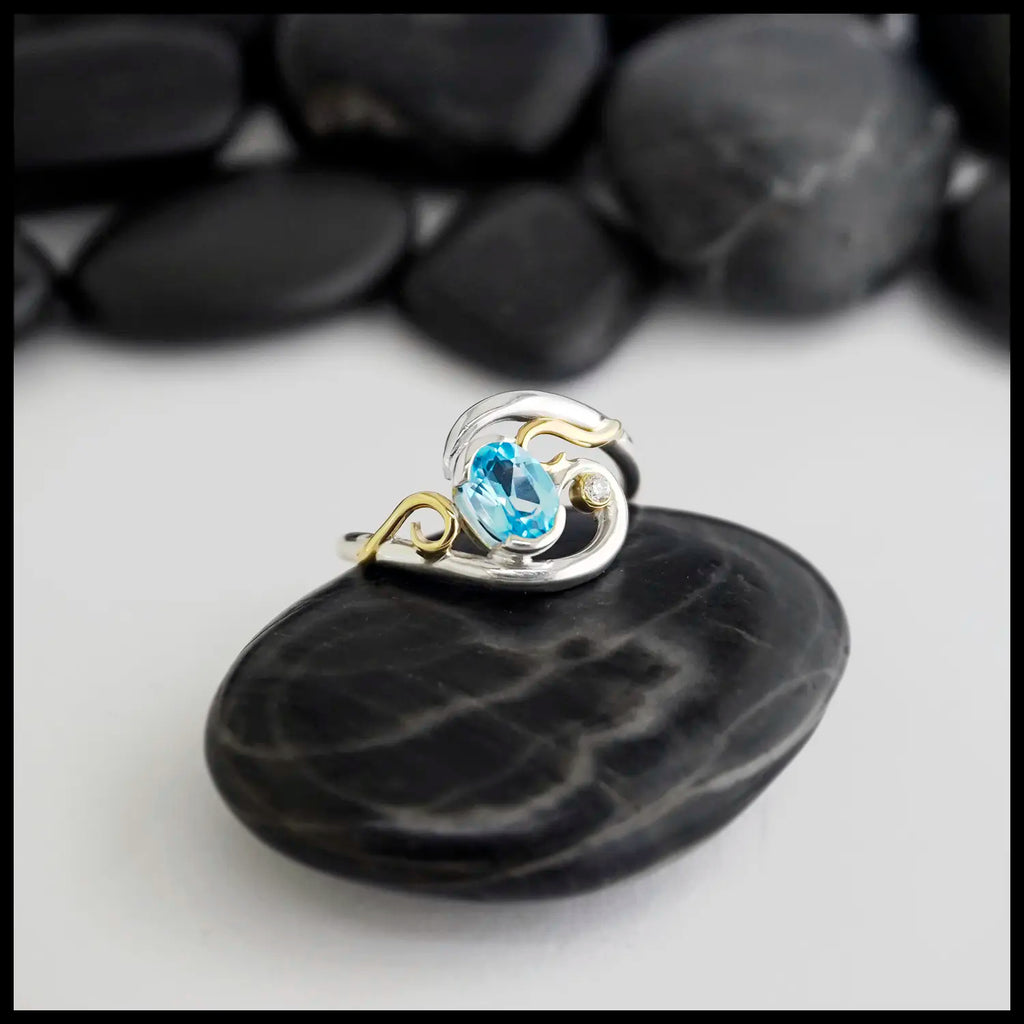 Silver and Yellow Gold ring with a blue topaz & diamond on a black stone with a blurred background