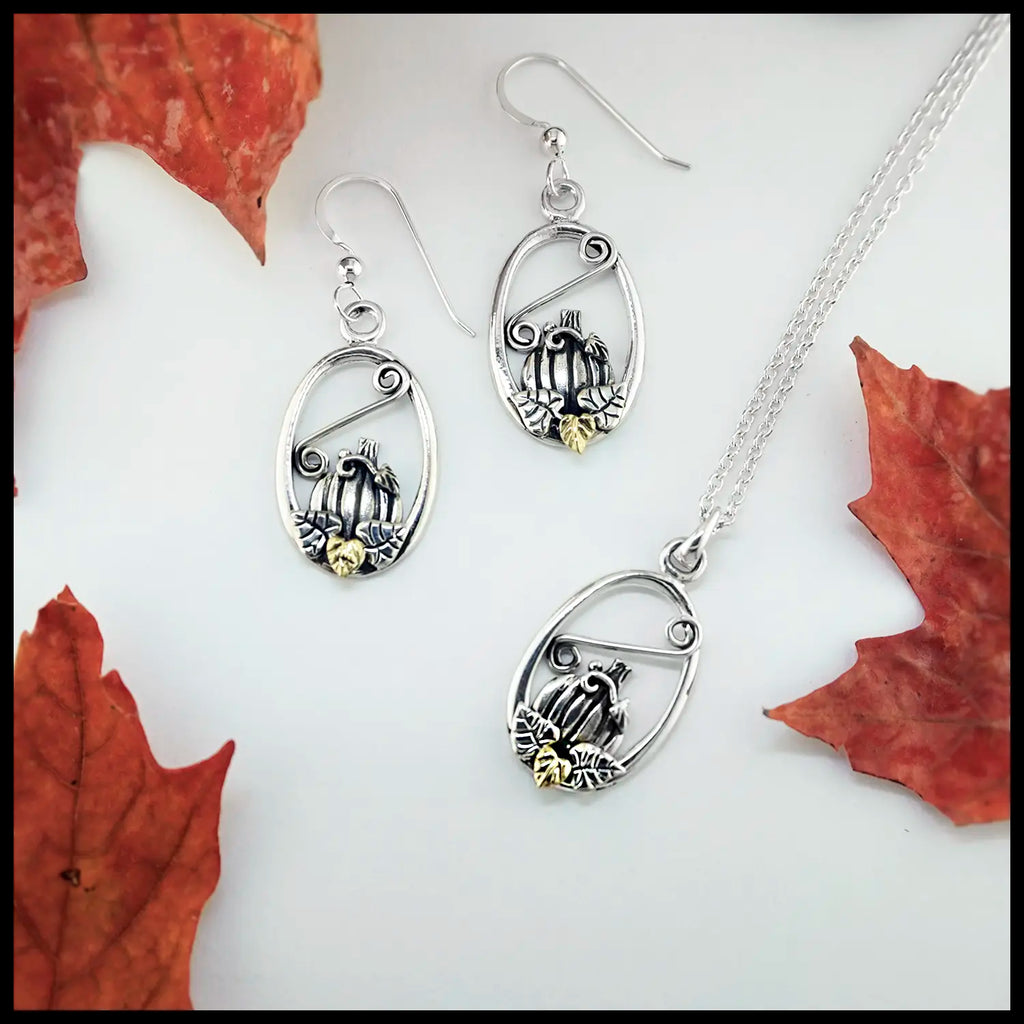 Silver jewelry pumpkin frame set with pendant and earrings with a 18K Yellow Gold Leaf, displayed on a white background with red leaves.