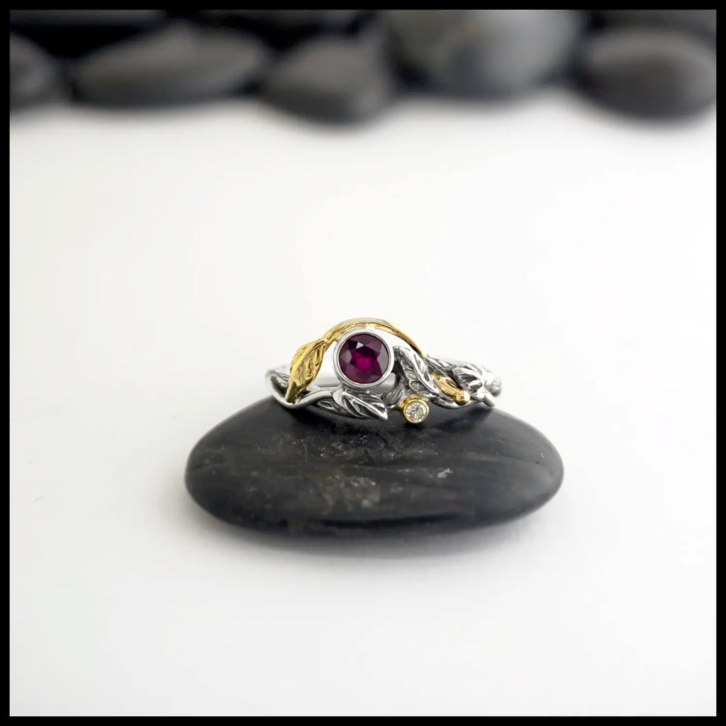 Silver and gold Leaf and Branch design ring with a red ruby and diamond, placed on a black stone