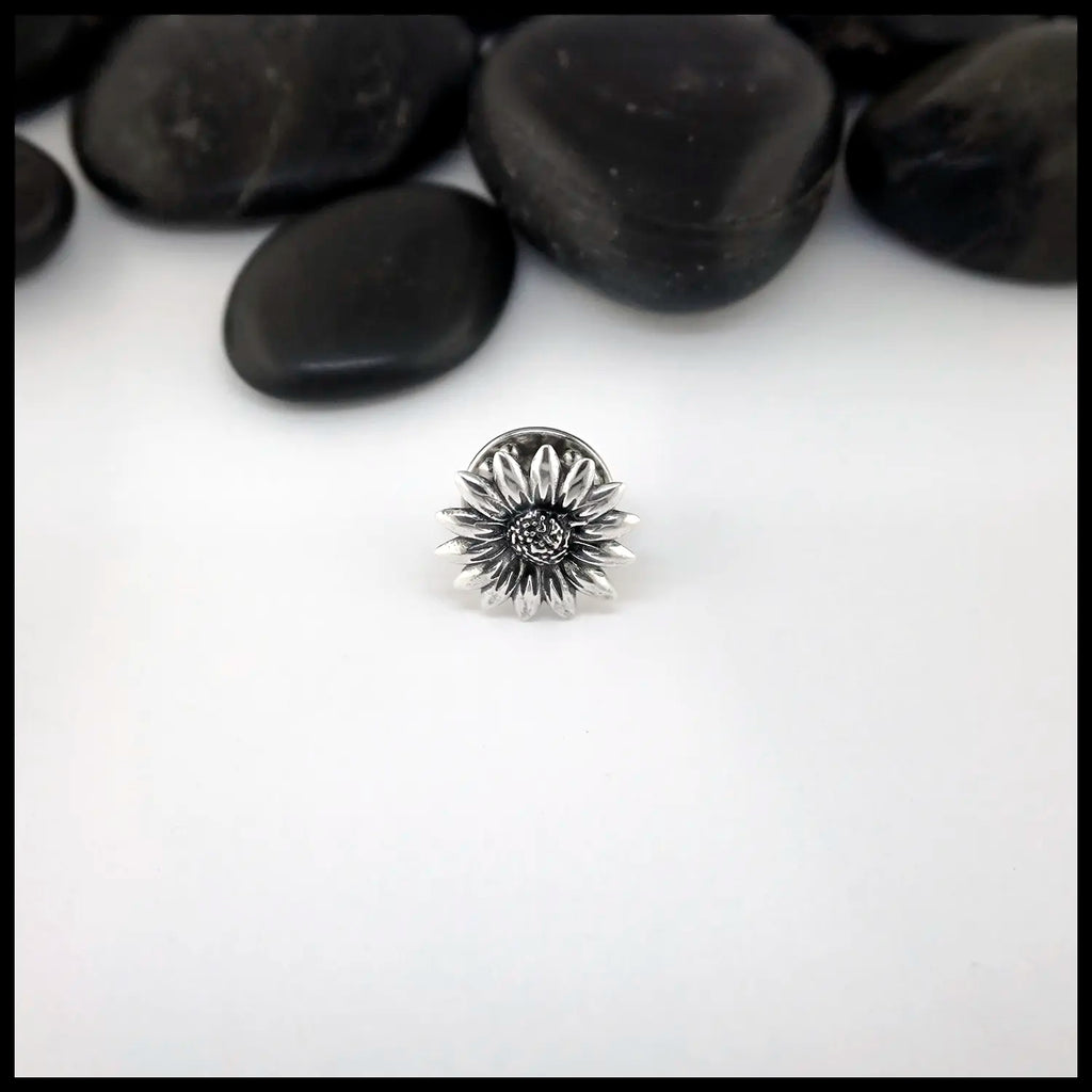 Silver flower-shaped Sterling Silver Pin on a white surface with black stones in the background