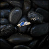14K Yellow Trinity Scroll ring with a blue sapphire Marquise and diamond pear set on black pebbles