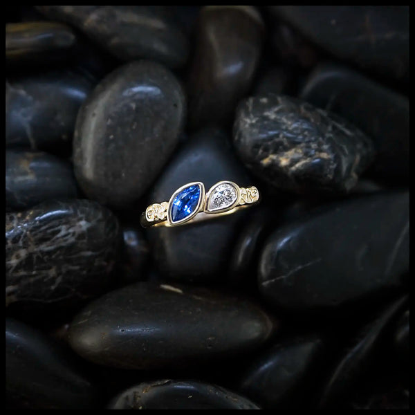 14K Yellow Trinity Scroll ring with a blue sapphire Marquise and diamond pear set on black pebbles