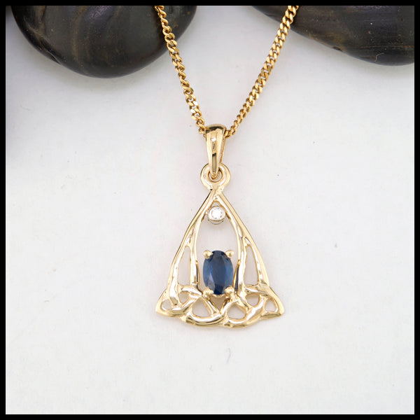 Gold pendant with a blue sapphire on a white background