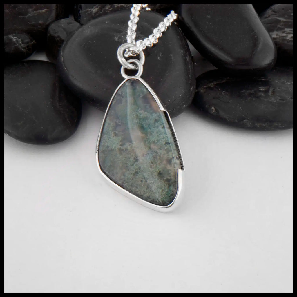 This custom Scalene Triangle Cabochon Moss Agate pendant is set in a custom open back, asymmetrical Sterling Silver Bezel. The backside, decorated with a 14 Karat Yellow Gold climbing spiral with the edges of the bezel. Includes an 18 inch Medium Rolo Chain.