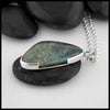 This custom Scalene Triangle Cabochon Moss Agate pendant is set in a custom open back, asymmetrical Sterling Silver Bezel. The backside, decorated with a 14 Karat Yellow Gold climbing spiral with the edges of the bezel. This photo includes a side shot of the pendant to show off the asymmetrical bezel with the break in the the frame to introduce a fork like pattern. Includes an 18 inch Medium Rolo Chain.