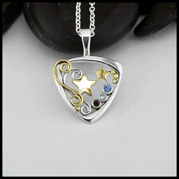 A Sterling Silver Downward facing Triangular Frame with two 14 Karat Yellow Gold alternating Stars in the center.  Silver and a Gold Double Swirl accenting the Right side of the pendant.  Evenly placed around the frame, are some 14 Karat Yellow Gold Beads. On the left side there are a bezel set Sapphire, Diamond and Ruby. In that order. To symbolize the colors of the American Flag. This pendant is called The Liberty Star Pendant & was made by our Craftsman Sydney. This pendant includes an 18" Cable Chain.