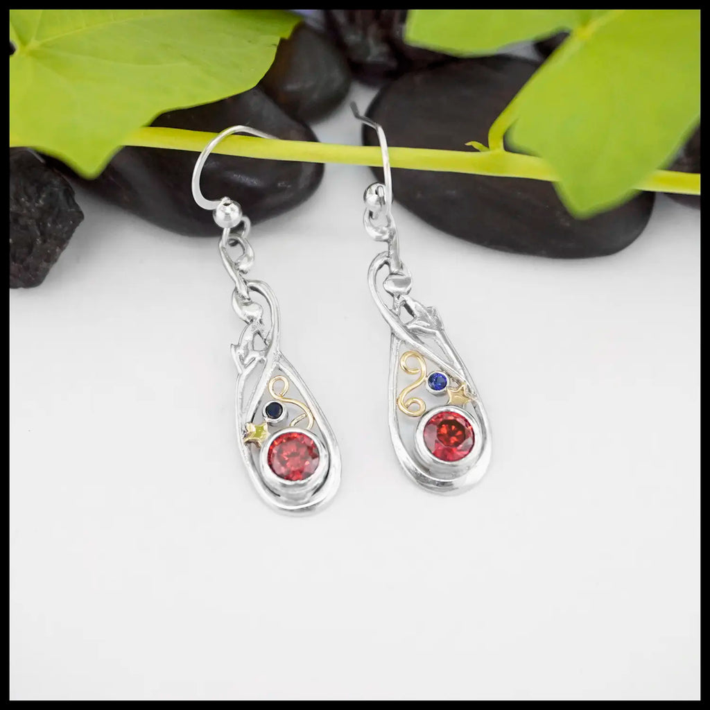 Sterling Silver Nouveau Fleur Frame Drop Earrings with a 5mm Synthetic Garnet and a 2mm Synthetic Sapphire. combining the two stones in the center are a 18K Yellow Gold Swirl and Star. Giving it that Fire Cracker Flare. Fresh off of Terry's Bench.