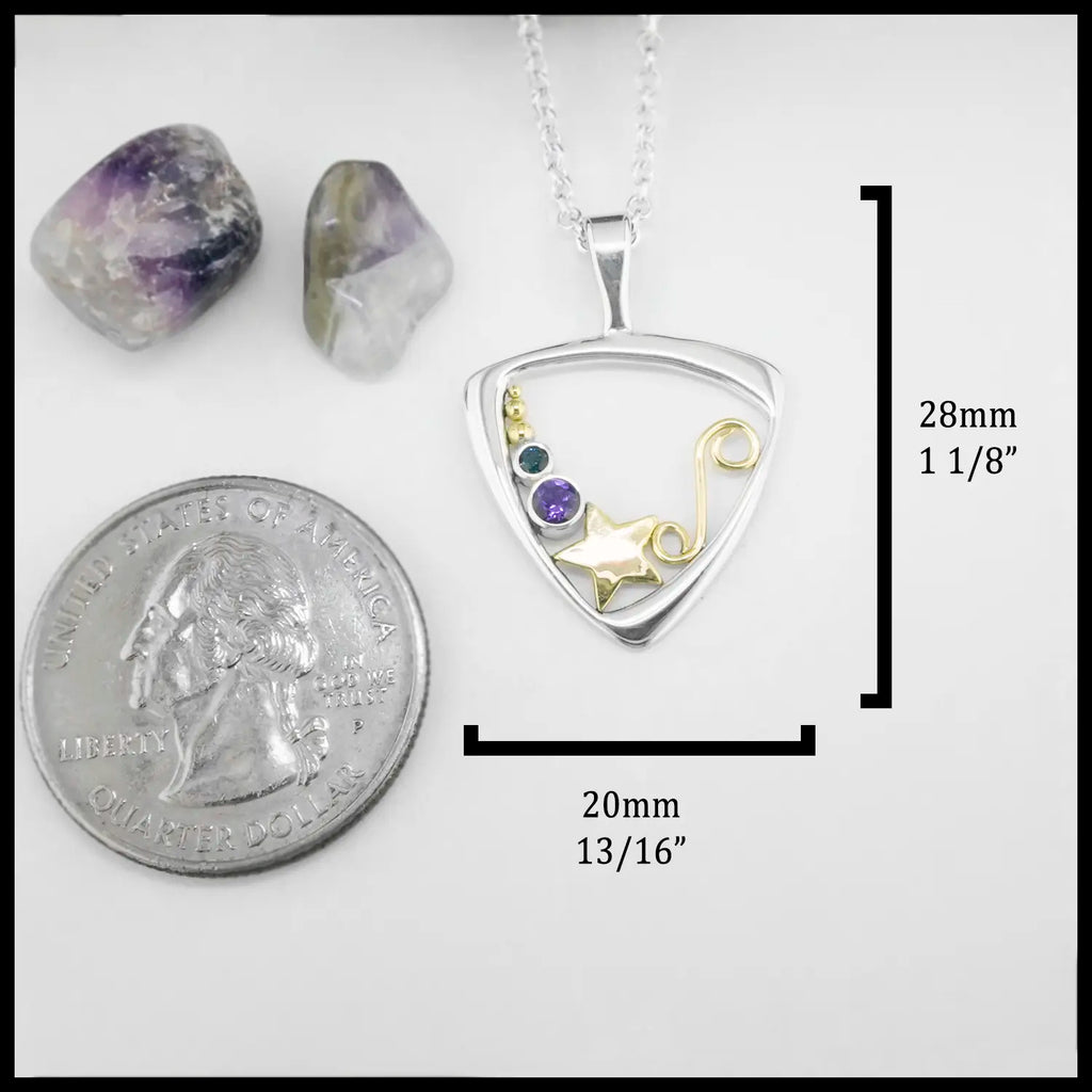 Triangular frame pendant with star and swirl design, with blue and purple stone settings. Surrounded by stones and a quarter for scale on a white background.