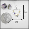 Triangular frame pendant with star and swirl design, with blue and purple stone settings. Surrounded by stones and a quarter for scale on a white background.