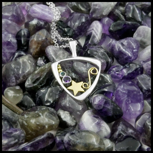 Triangular frame pendant with star and swirl design, with blue and purple stone settings. Draped over a bed of purple amethyst stones