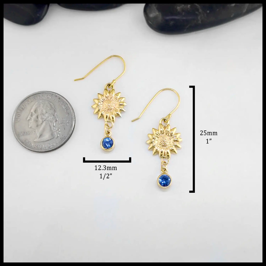 Gold sunflower earrings with Tanzanites on a white background, shown with a quarter for scale. The measurements of these earrings are: 25mm or 1 inch Tall and 12.3mm or 1/2 inch Wide.