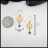 Gold sunflower earrings with Tanzanites on a white background, shown with a quarter for scale. The measurements of these earrings are: 25mm or 1 inch Tall and 12.3mm or 1/2 inch Wide.