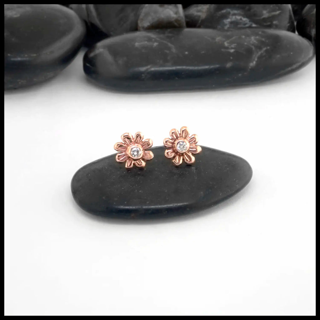 Rose gold flower-shaped earrings with a central Diamond on a black stone background
