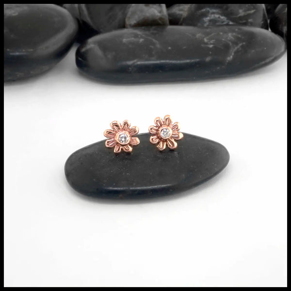 Rose gold flower-shaped earrings with a central Diamond on a black stone background
