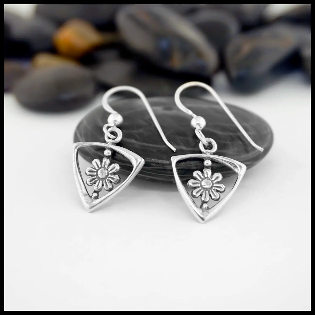 Sterling Silver Triangle Frame earrings with Daisy Design on a white surface with pebbles in the background