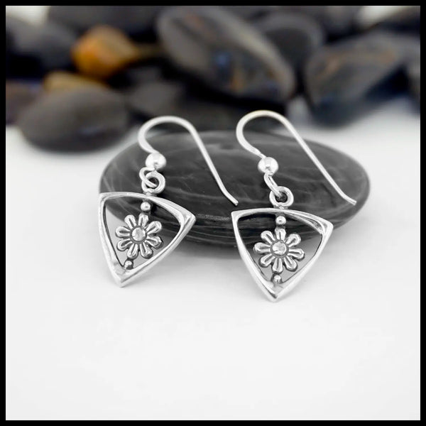Sterling Silver Triangle Frame earrings with Daisy Design on a white surface with pebbles in the background