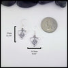 Silver triangle frame earrings with daisy designs on a white background with measurements and a coin for scale. Measurements: 17mm or 11/16" Tall and 14.5mm or 9/16" Wide.
