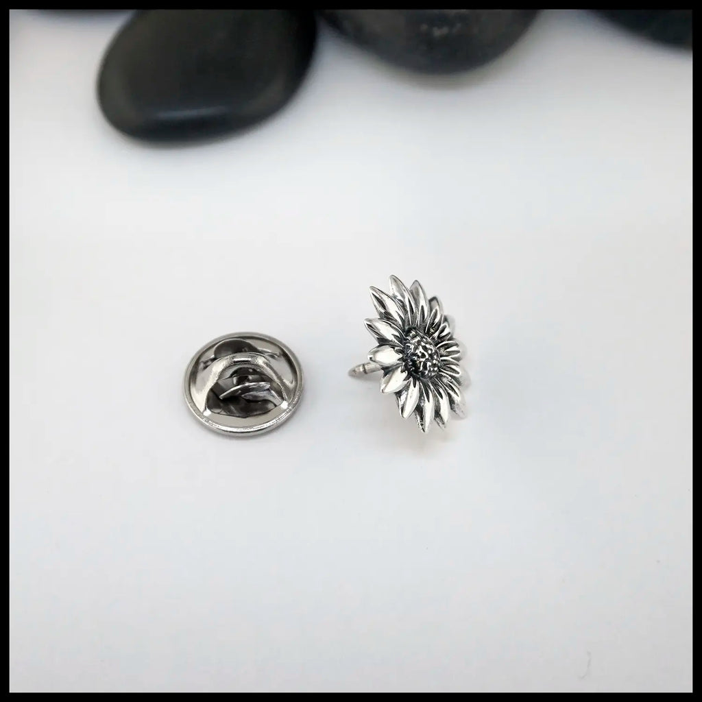 Silver flower-shaped Sterling Silver Pin on a white surface with black stones in the background