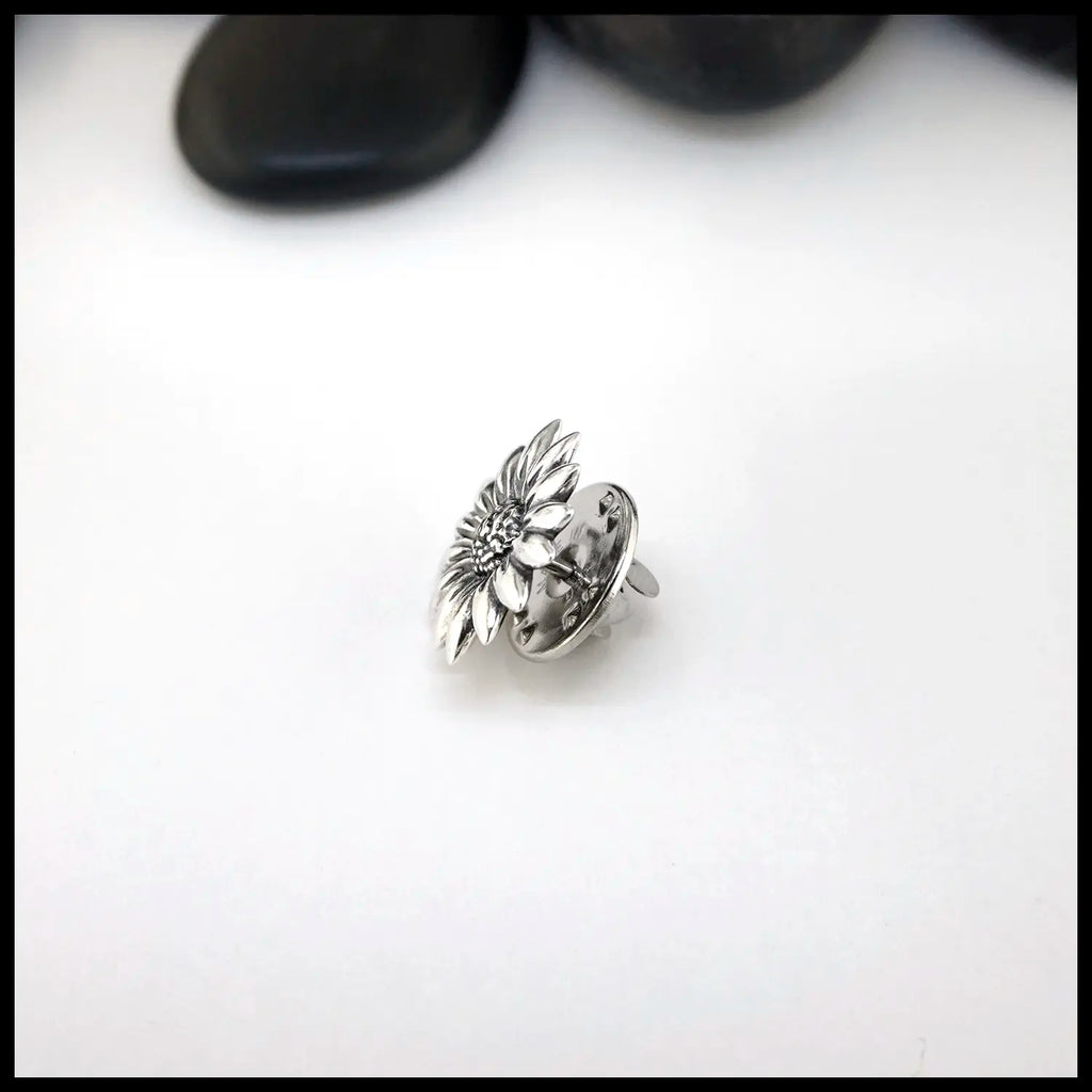 Silver flower-shaped Sterling Silver Pin on a white surface with black stones in the background
