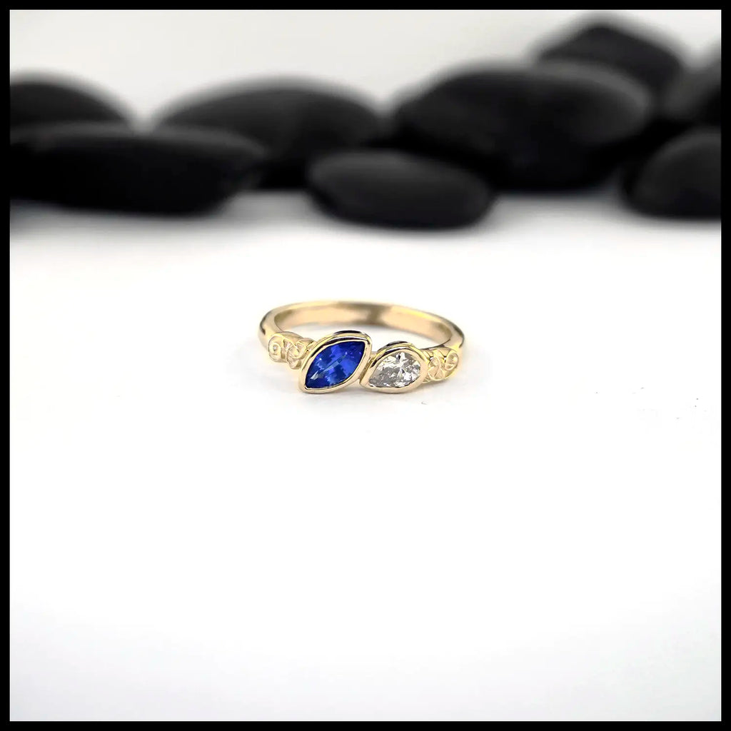 Gold ring with a Marquise Sapphire and a pear cut diamond on a white background