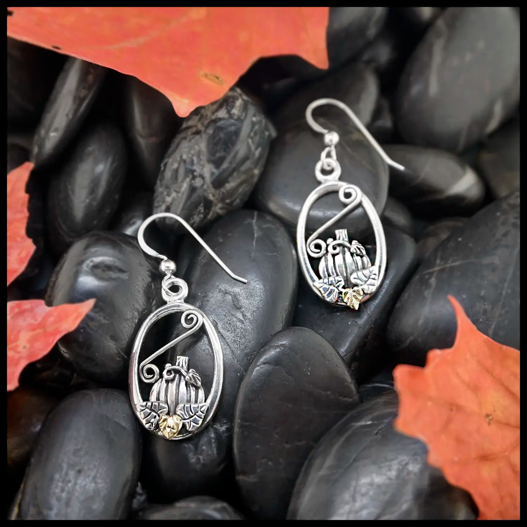 Silver pumpkin frame earrings with intricate designs on dark stones with autumn leaves