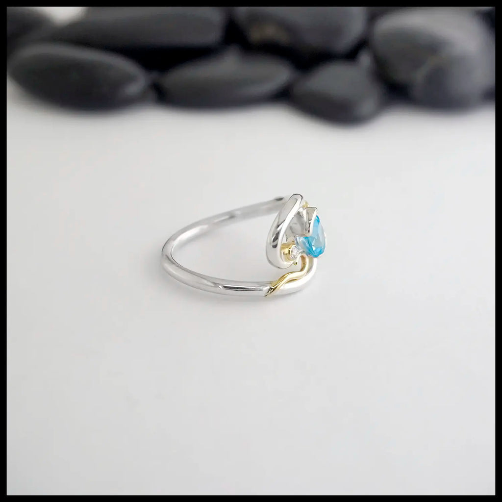 Silver ring with a blue topaz and diamond and gold accent on a light gray background