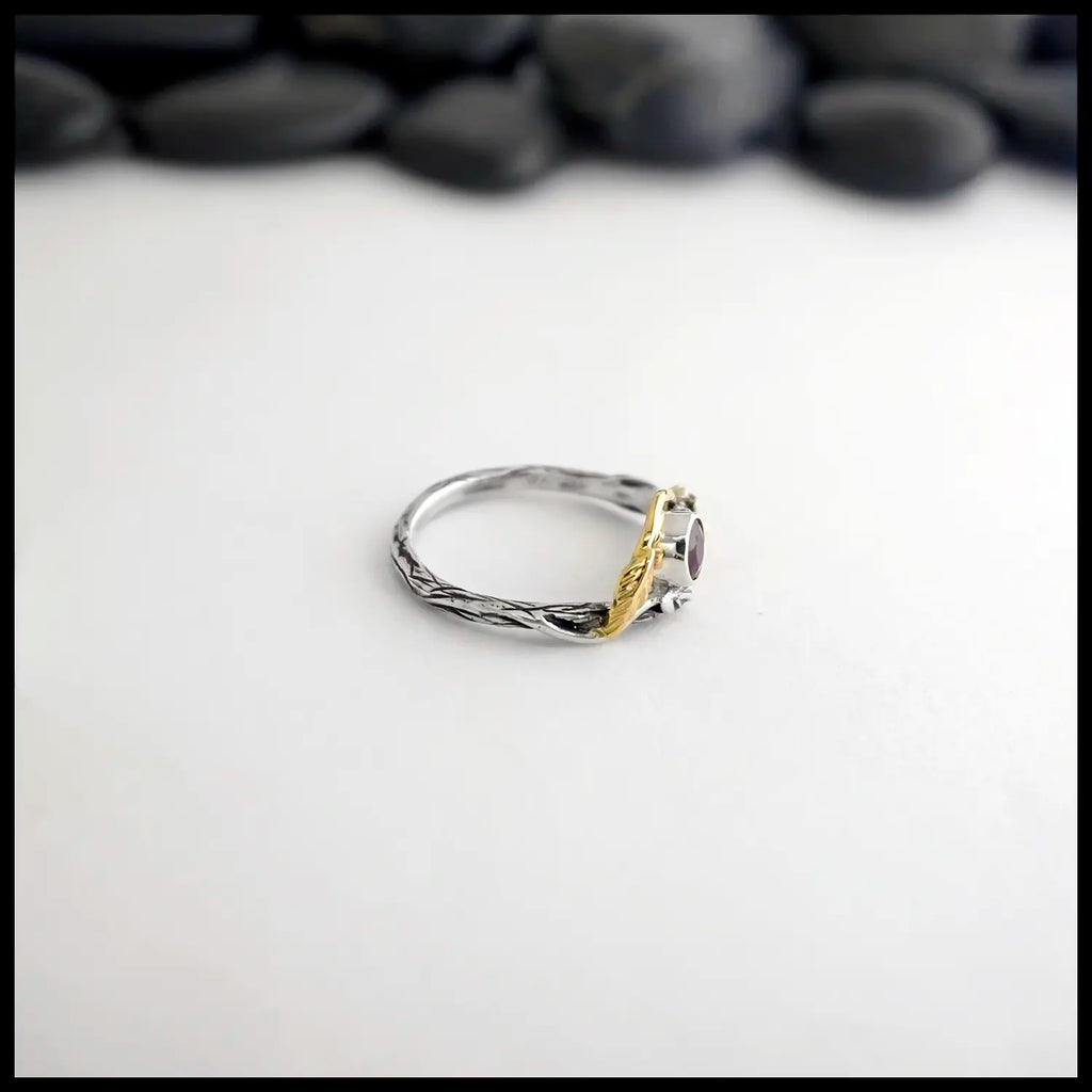 Silver and gold leaf and branch ruby ring on a white background with blurred stones in the background