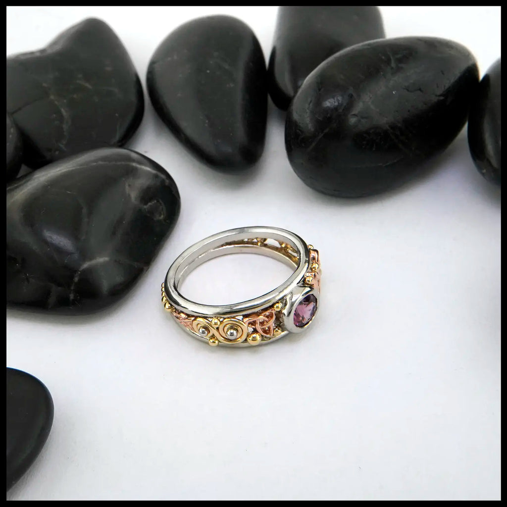 Multicolored ring with gemstone on a white surface with black stones in the background