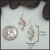 Silver earrings with gemstones on a white surface with a quarter for scale.