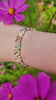 Three Sisters Link Bracelet in tri-color 14K gold worn on the wrist, shown outdoors among cosmos flowers.
