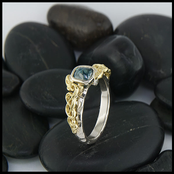 Profile view of 14K White Gold textured band with an 18K Yellow Gold cathedral design, set with a .59CT blue rose cut Diamond and a .06CT accent Diamond. 